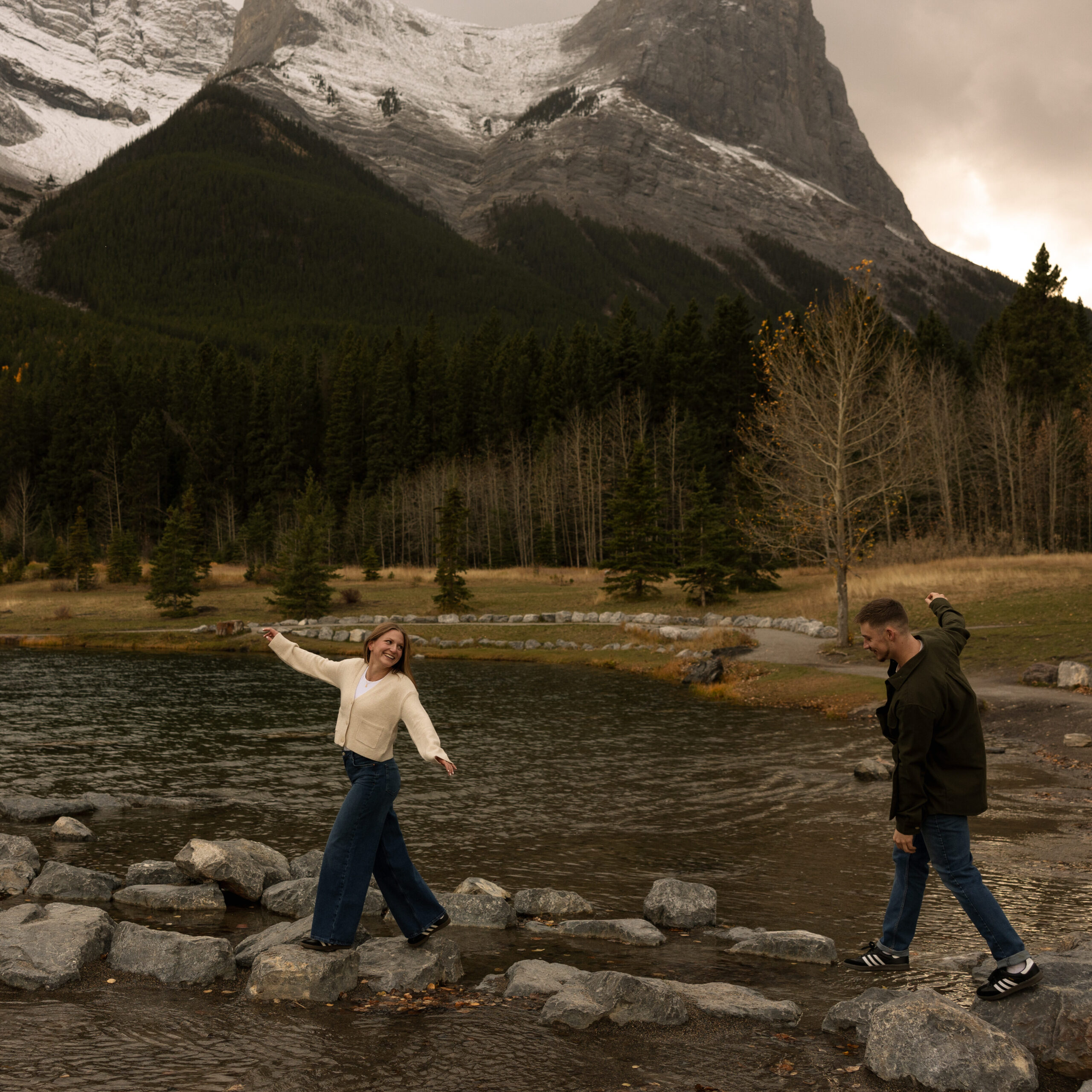 canmore engagement photos of couple playfully walking on rocks in quarry lake, canmore