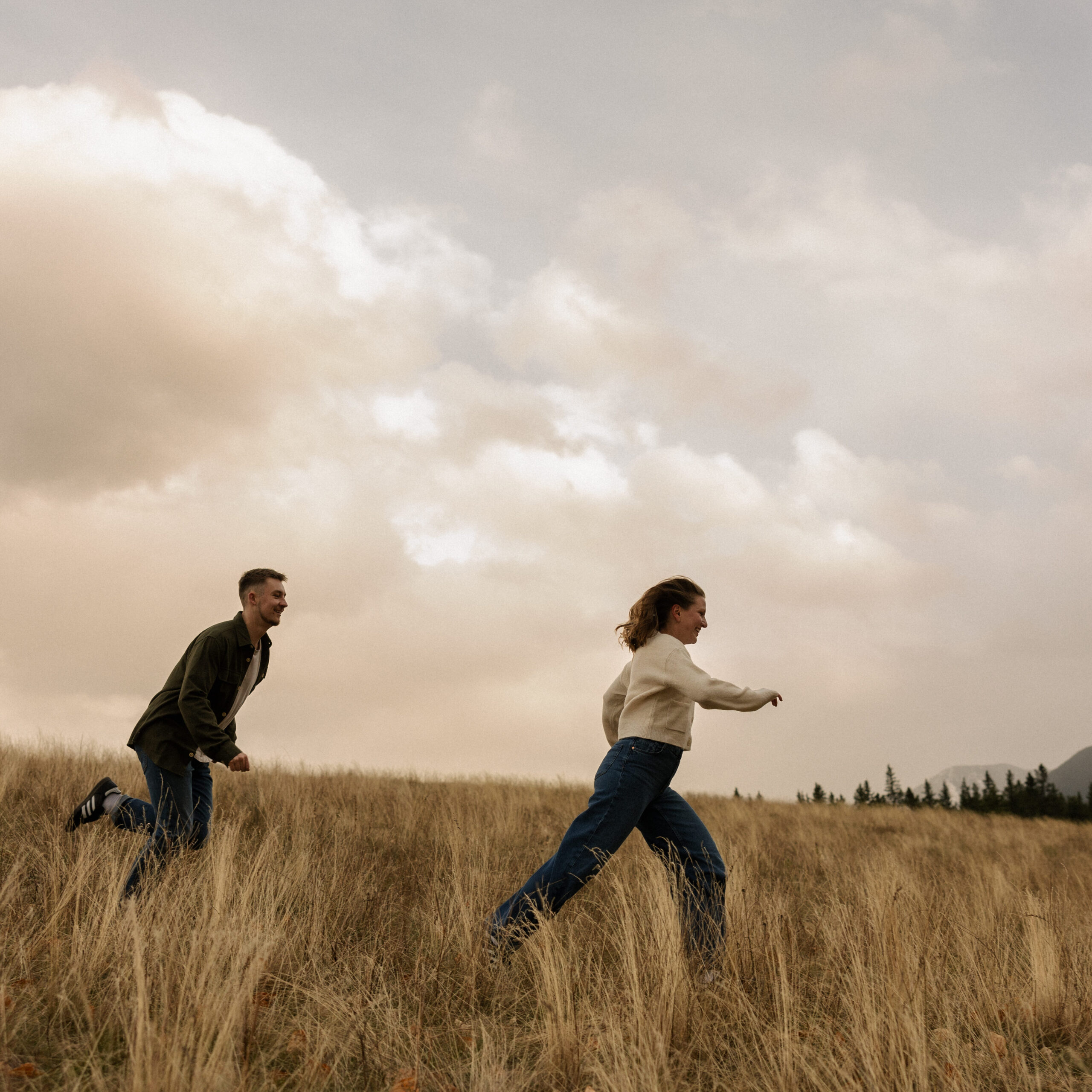 storytelling canmore engagement photo of couple running around a field surrounded by mountains in canmore, alberta danielle boulger photography